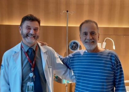 Homem de 61 anos sorrindo ao lado de seu médico em um ambiente hospitalar, celebrando a recuperação de sua saúde.