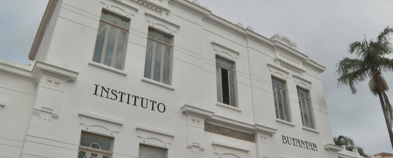 Cientista de jaleco branco utilizando uma pipeta de precisão para manipular amostras em tubos de ensaio dentro de um laboratório de virologia moderno.