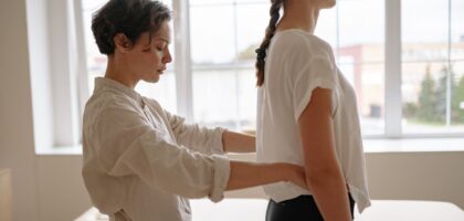 Uma mulher de cerca de 55 anos sentada de forma ereta em uma cadeira de escritório, realizando um alongamento do pescoço ao inclinar a cabeça para o lado.