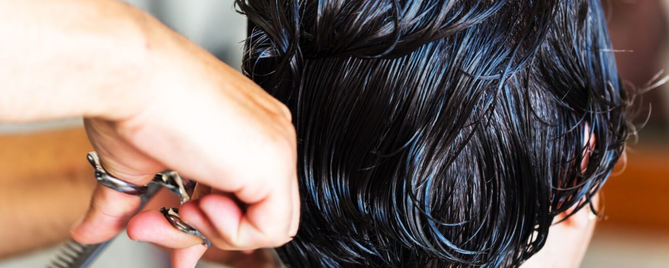 Mulher de cinquenta anos olhando preocupada para uma escova de cabelo com fios caídos em um banheiro iluminado.
