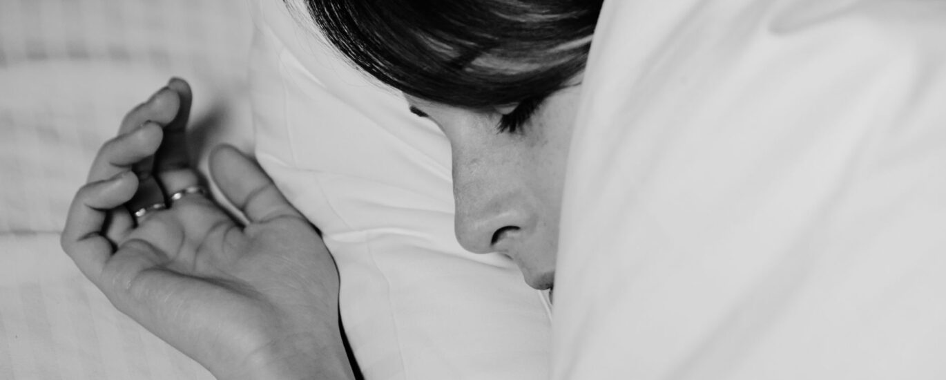 Homem de meia-idade sentado na beira da cama à noite, massageando a panturrilha com expressão de desconforto sob uma luz suave de abajur.